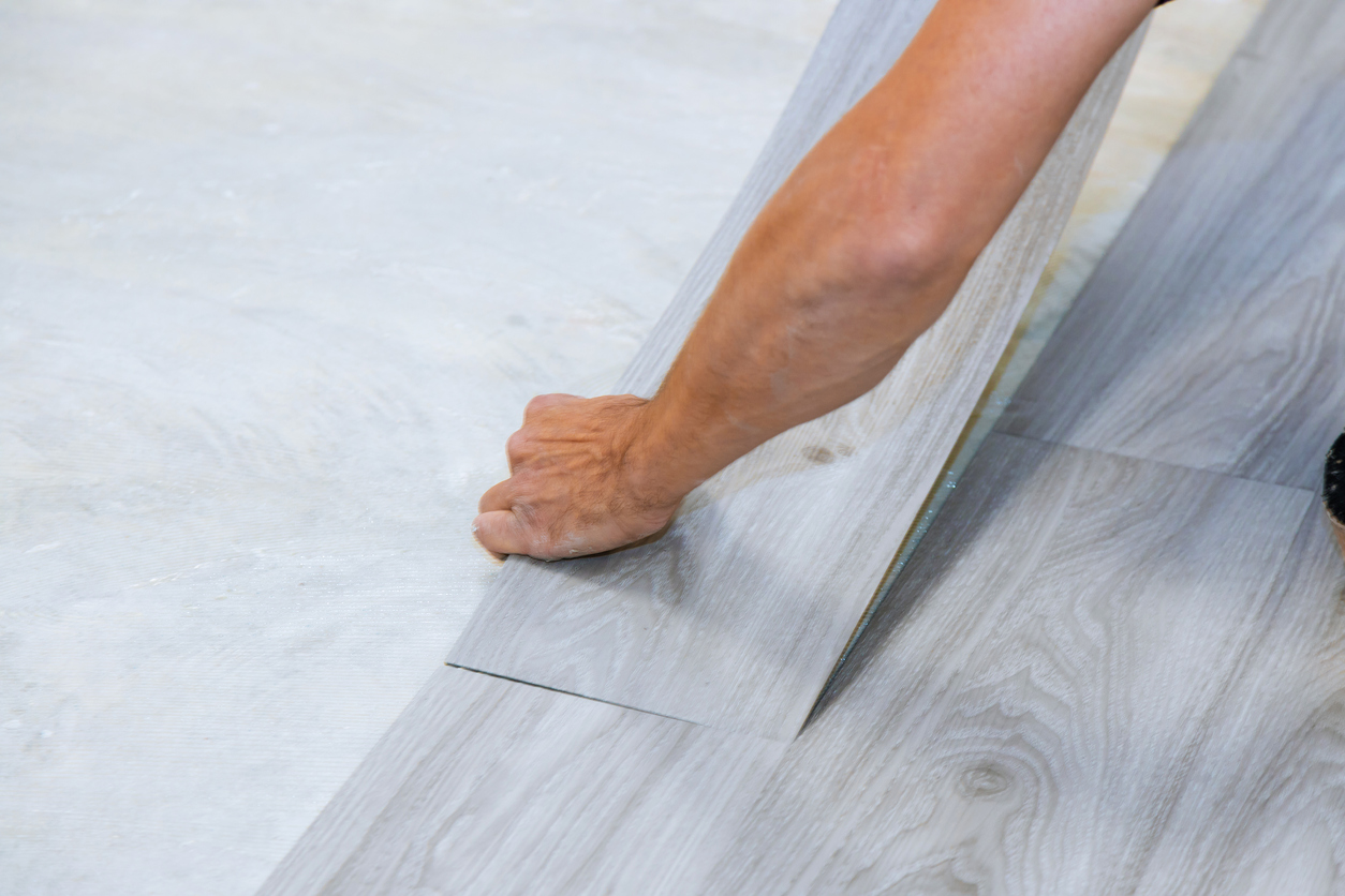 Worker installing new vinyl tile floor with new home improvement laminate wood texture floor